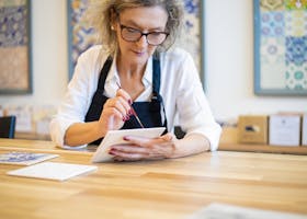 Senior woman painting a tile in Portugal, showcasing artistic passion and creativity in a focused setting.